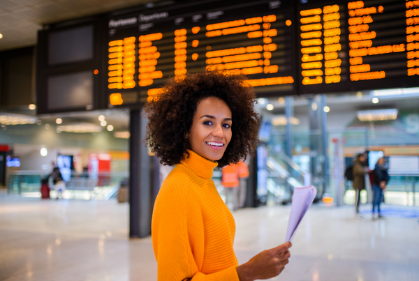 Mulher negra segurando um papel e sorrindo para a câmera em saguão de aeroporto.