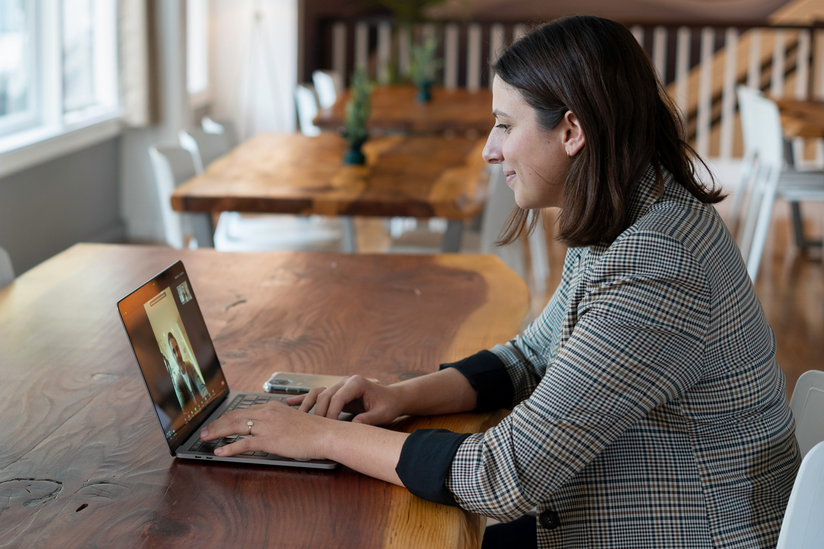 Mulher sentada em uma mesa vista de perfil enquanto está em uma reunião online