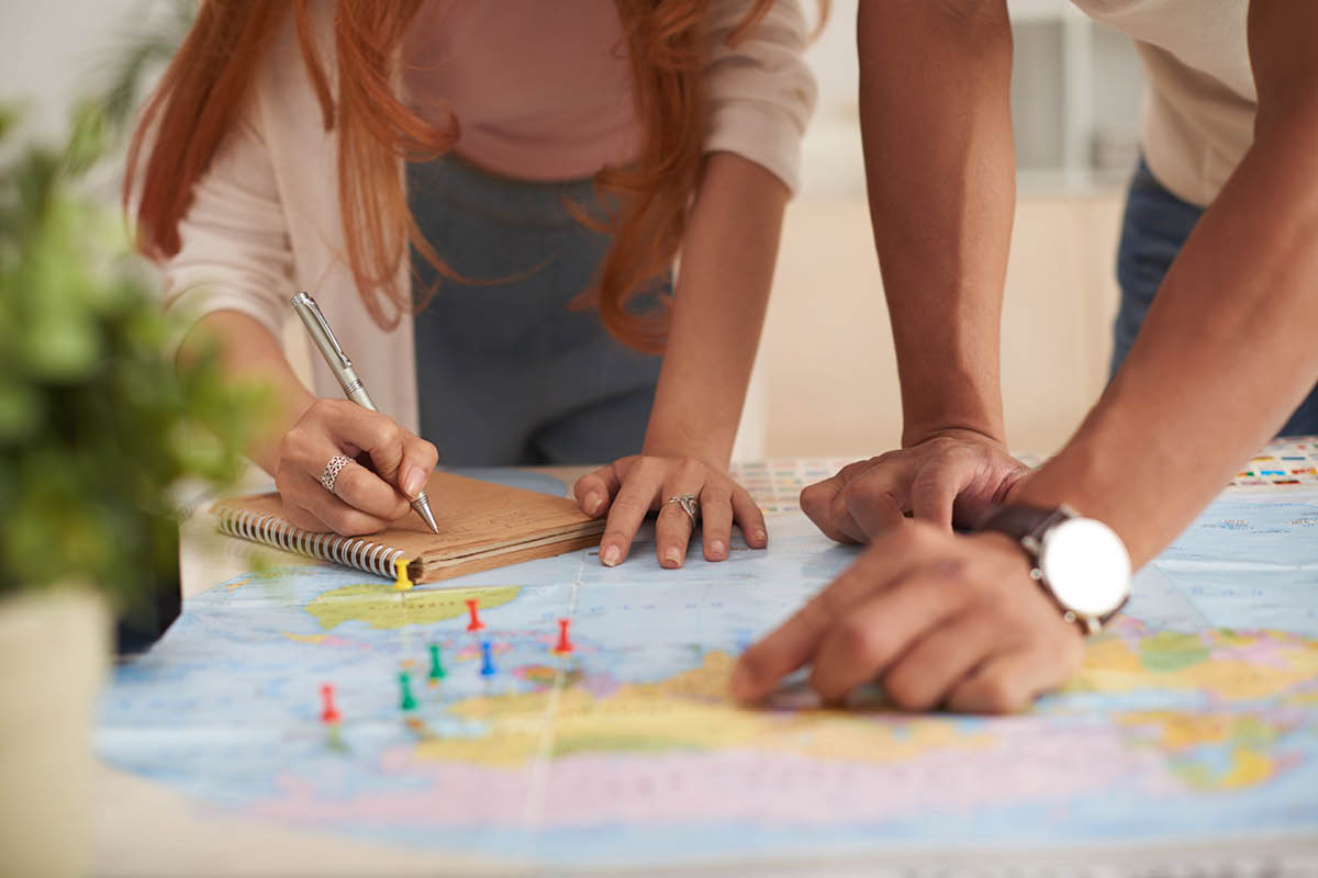 Duas pessoas, inclinadas sobre um mapa mundial, planejando uma viagem